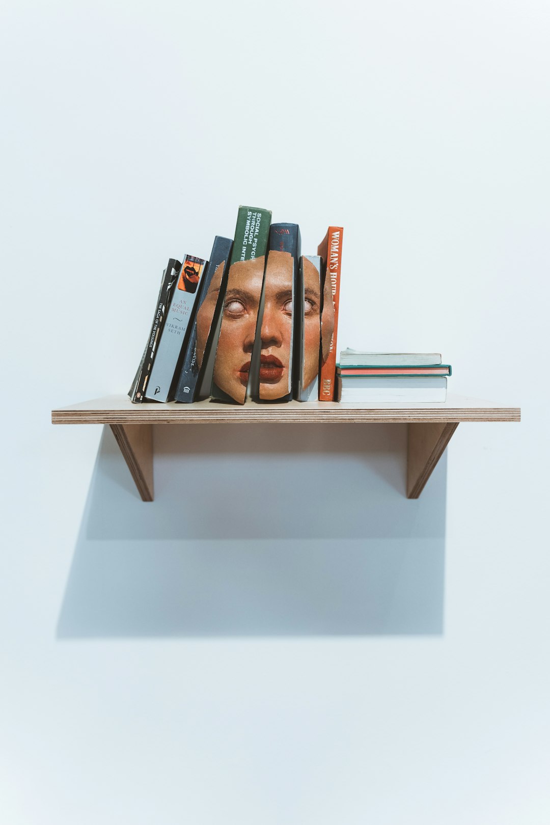 book shelf on white wall with a picture of a face on the spines of the books