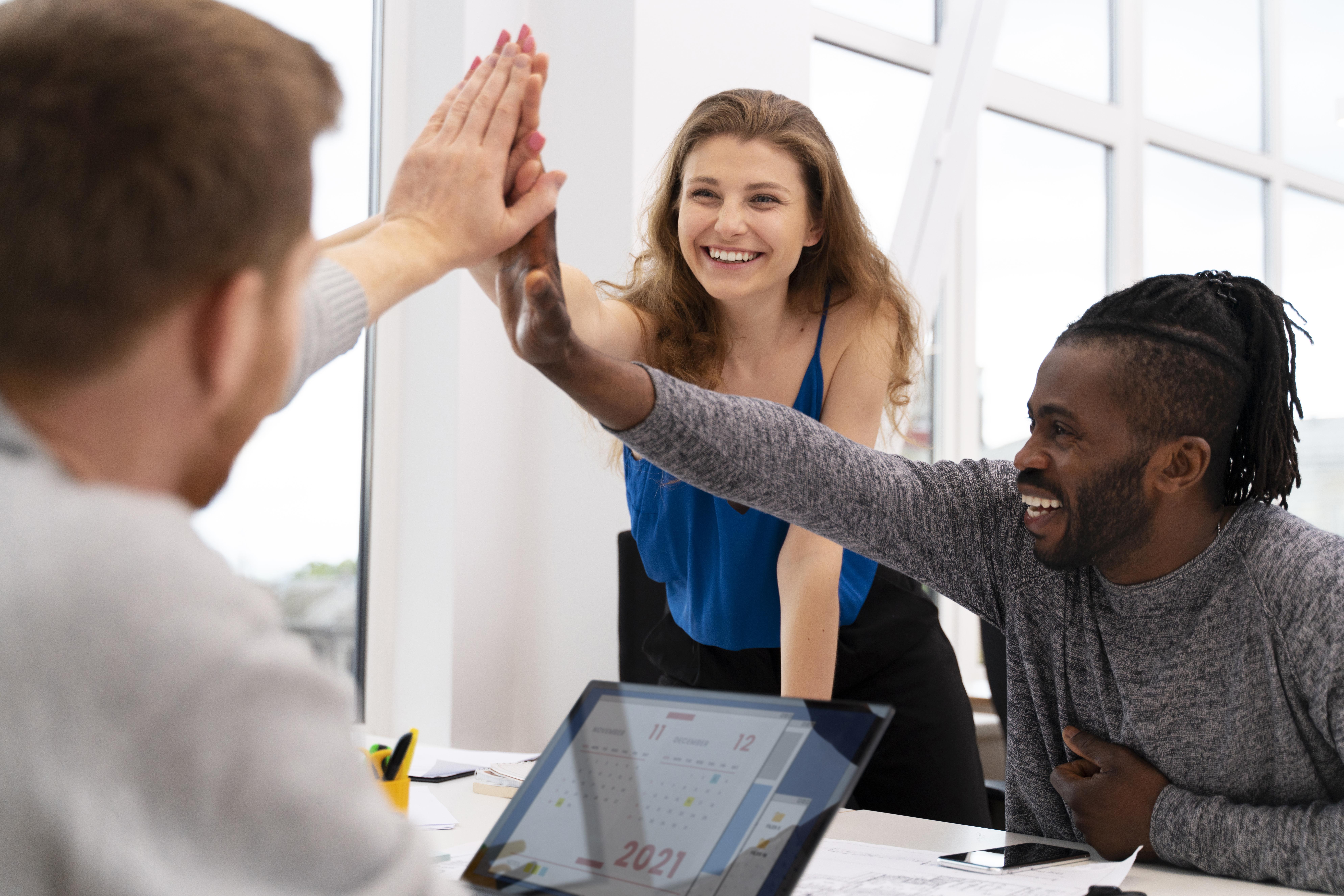 team of 2 men and 1 woman doing a High Five over a desk.